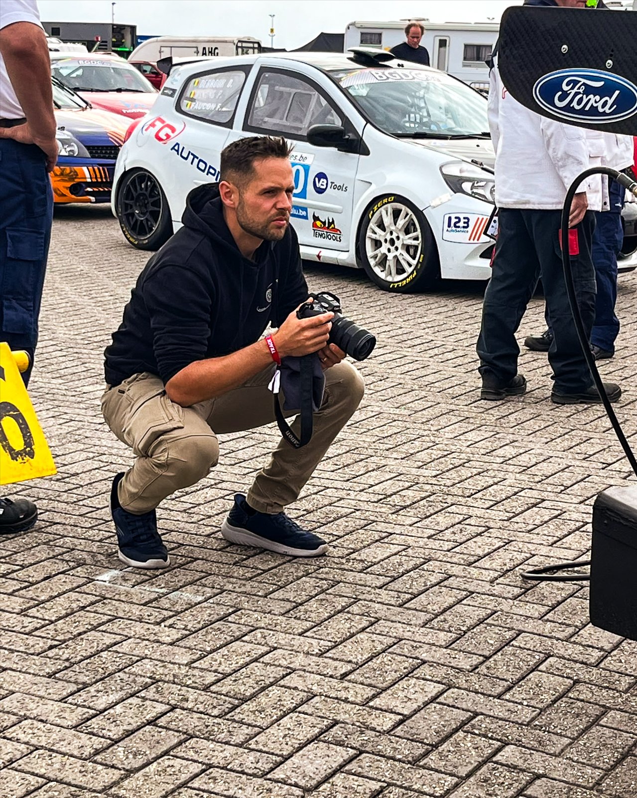 Arnaud accroupi dans le paddock, appareil en main, entre les voitures du BGDC
